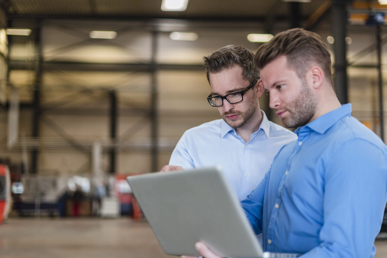 Two businessmen sharing laptop on factory shop floor