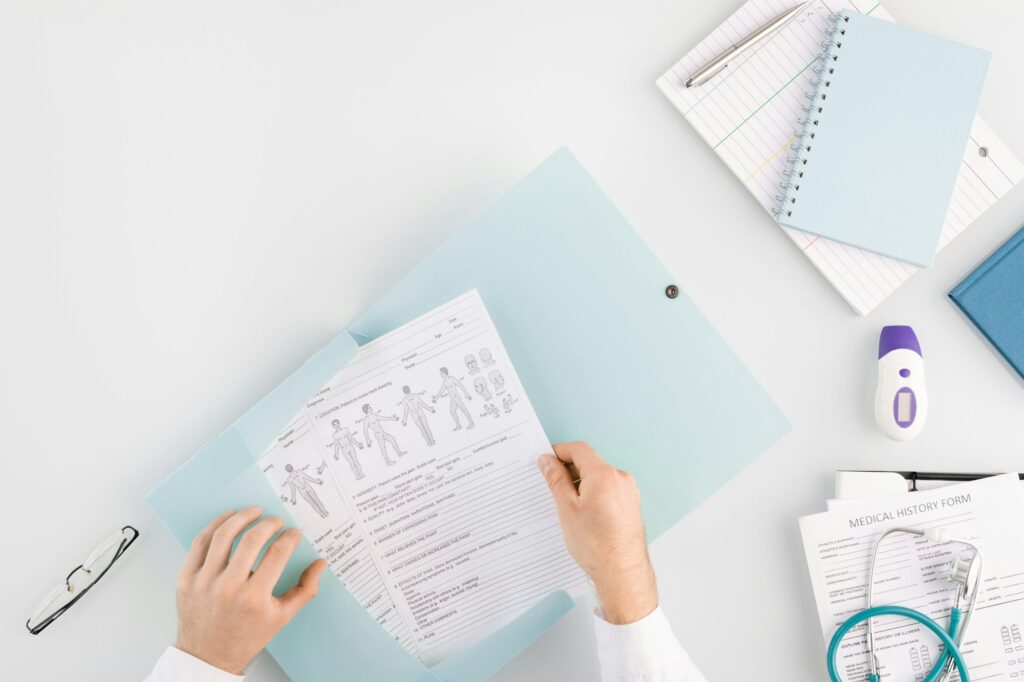 Hands of doctor putting medical document into folder with other files on table