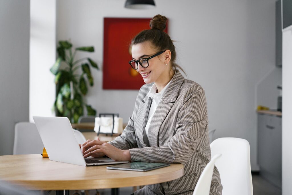 In a bright workspace, a smiling professional in smart attire efficiently works on her laptop, addin