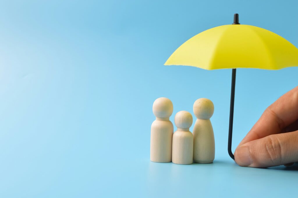 Yellow umbrella and wooden doll figures. Insurance coverage concept.