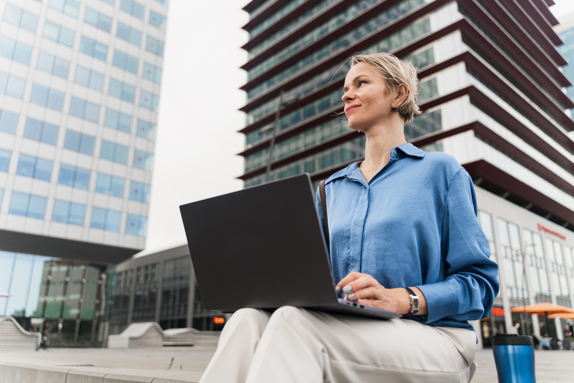 Blond business woman working on laptop sitting outside office building